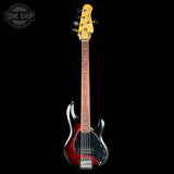 Electric bass guitar with a red and black body on a black background, featuring the Tone Shop logo.