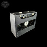 A vintage black guitar amplifier with its front speaker grille removed, showing the internal speaker and control knobs, photographed against a solid black background.