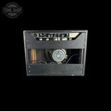 A vintage black guitar amplifier head with a textured cabinet, showing the internal speaker and control panel through a glass front, photographed against a solid black background.