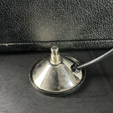 A silver metallic cone-shaped suction cup with a black rubber base and a black cable, shown on a dark textured surface.