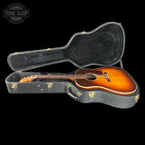Acoustic guitar in a hard-shell case with 'Tone Shop' logo in the corner.