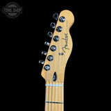 Close-up of a Fender Telecaster electric guitar headstock and upper neck, showing the maple wood headstock, six tuning pegs, and black Fender branding, set against a solid black background.