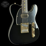 Black electric guitar with gold hardware on a black background, featuring 'Tone Shop' logo.
