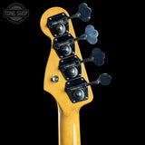 Close-up rear view of a bass guitar headstock with four black four-leaf tuning pegs and black tailpiece covers on a yellow-orange wood finish, shown against a black background.