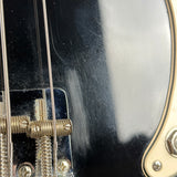 Close-up detail of a black electric guitar body showing the bridge, strings, and part of the cream-colored pickguard.