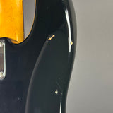Close-up of a glossy black electric guitar body with visible wear, scuffs, and small gold-colored metal components near the edge, set against a plain gray background.