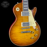 A close-up of a Gibson Les Paul Custom electric guitar body in a natural sunburst finish, featuring a cream pickguard, dual humbucker pickups, and gold-toned hardware, set against a solid black background with a Tone Shop watermark in the top left corner.