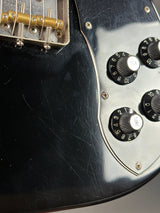 Close-up of a black electric guitar with control knobs and tuning pegs.