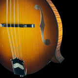 Close-up of a hollow-body acoustic guitar body showing the sunburst finish, f-hole, bridge, strings, and part of the carved back against a black background.