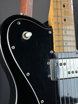 Close-up of a black electric guitar with visible hardware and wood finish.