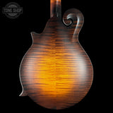 Close-up of the back of a mandolin with a glossy natural wood finish showing a vibrant amber glow and detailed grain patterns against a black background.
