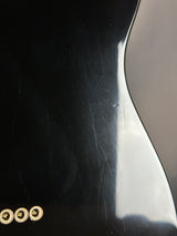 Close-up of a black guitar with visible scratches and a gold tuning peg.