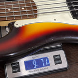 A close-up of a sunburst electric bass guitar body resting on a digital scale showing 9.1 lbs, with part of the neck and pickups visible.