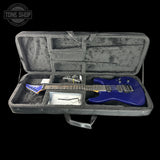 A blue electric guitar displayed inside an open gray hard case on a black background, with accessories and a Tune Shop logo watermark visible.