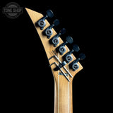Close-up of the headstock of a Gretsch electric guitar with a natural wood finish, black tuning pegs, and a hex key inserted for truss adjustment, set against a solid black background.