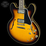 A classic double-cutaway electric guitar with a sunburst finish, featuring a black pickguard, chrome hardware, and gold control knobs, shown against a solid black background with a Tone Shop watermark in the top left corner.