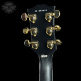 Close-up of the headstock of a Gibson electric guitar, showing six gold tuning pegs on a glossy black headstock against a black background.