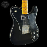 Black electric guitar with a worn finish on a black background, featuring the Tone Shop logo.