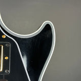 Close-up of a black electric guitar body with a white double stripe border and gold hardware against a dark gray background.