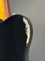 Close-up of a black guitar with a visible scratch on the body against a gray background.