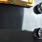 Close-up of a glossy black appliance surface with visible scratches and reflections, plus part of a gold control trim and black rotary knobs at the top and right.