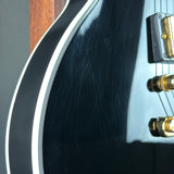 Close-up of a glossy black electric guitar body with white binding, showing visible scratches on the finish and part of a gold hardware component.
