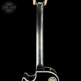 Close-up rear view of a black Gibson electric guitar body and neck, with white binding and a gold Gibson logo, shown against a black background.