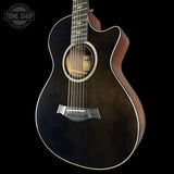 Acoustic guitar with a dark finish on a black background, featuring the Taylor brand.