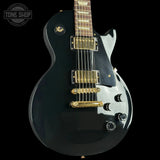 Black electric guitar with gold hardware on a black background, featuring 'Tone Shop' logo.