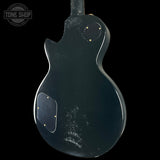 Black electric guitar body with visible wear on a black background, featuring 'Tone Shop' logo.
