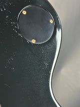 Close-up of a black guitar with a circular control knob and gold screws.