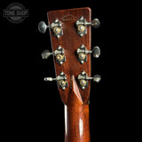 Close-up of the headstock of a Martin D-2150 Grand Auditor acoustic guitar, showing the rich reddish-brown wood grain and ornate silver-and-gold tuning pegs against a solid black background.