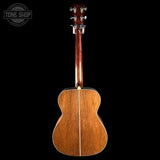 The back of a wooden acoustic guitar with a glossy reddish-brown finish and a central soundhole, shown against a solid black background with a Tone Shop watermark in the top left.