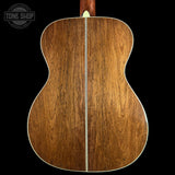 The back of an acoustic guitar made of rich brown wood with a central soundhole and a white binding edge, shown against a solid black background with a Tone Shop watermark in the top left.
