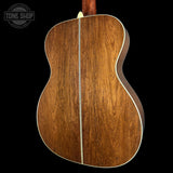 The back of an acoustic guitar made of rich brown wood with a central cream-colored inlay, shown against a solid black background with a Tone Shop watermark in the top left.