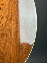 Close-up of a polished wooden instrument body edge with a glossy finish, showing warm brown wood grain against a dark gray background.
