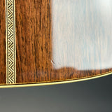 Close-up detail of a wooden instrument body showing rich brown wood grain, a decorative gold geometric inlay, and part of a light-colored soundboard.