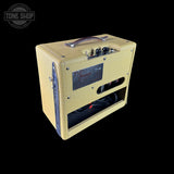A vintage-style guitar amplifier cabinet with a cream-colored textured grille cloth, a purple handle, and a black front speaker grille, shown against a solid black background.