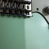 Close-up of a mint green electric guitar body showing the bridge, saddles, and part of the white pickguard.