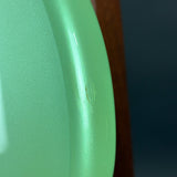Close-up of a mint green metallic surface with a small embossed logo, next to a dark brown vertical element and a dark blue background.