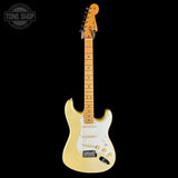 A classic Fender Stratocaster electric guitar in a pale gold finish, featuring a white pickguard and maple neck, shown against a solid black background with a Tone Shop watermark in the top left corner.