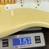 Close-up of a cream-colored electric guitar body resting on a digital scale displaying its weight of 7.157 lbs.