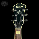 Close-up of the headstock of an Ibanez guitar on a black background, showing the Ibanez logo, model name, tuning pegs, and part of the fretboard.