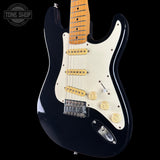 Black electric guitar with a white pickguard on a black background, featuring the Tone Shop logo.