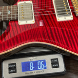 Red electric guitar on a digital scale displaying weight.