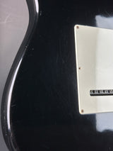 Close-up of a black electric guitar with a gold pickguard.