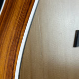 Close-up of a guitar body showing a dark brown wood veneer edge, a white binding strip, and a beige textured backplate with a single visible scratch.