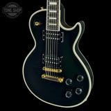 Black electric guitar with gold hardware on a black background, featuring 'Tone Shop' logo.
