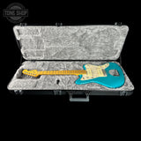 An electric guitar with a turquoise body and yellow neck displayed inside an open padded hard case on a black background. A Tone Shop watermark is visible in the top-left corner.
