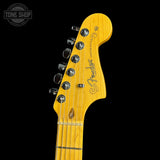 Close-up of a Fender electric guitar headstock in a natural maple finish, showing six silver tuning pegs and the Fender logo, set against a solid black background.